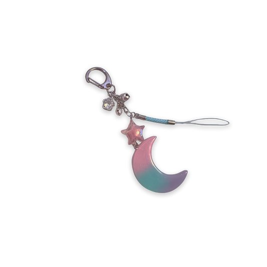 Specialty keychain featuring a sparkly resin moon charm with pastel colors and connecting star charm, with small bells and crystal flower charm and braided phone strap.