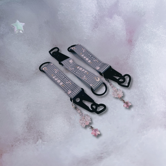 Soft but deadly key straps feature black metal detailing and black heart carabiner, with special bow keychain attached, and strap featuring "soft but deadly" text on a light grey pattern.