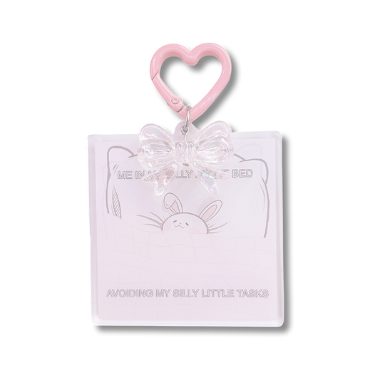 Bunny in Bed Acrylic Keychain design features a bunny in bed with text "Me in a silly little bed avoiding my silly little tasks," with a heart carabiner and clear bow attached.