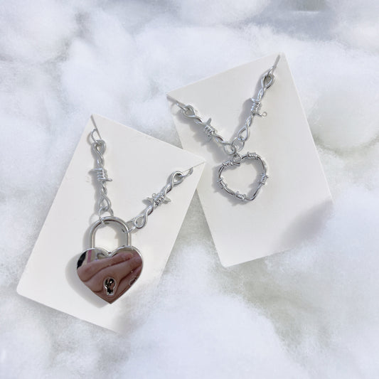 Silver Heart Locket Necklace with barbed necklace chain necklace displayed on the left, silver heart charm with barbed necklace chain necklace on the right.