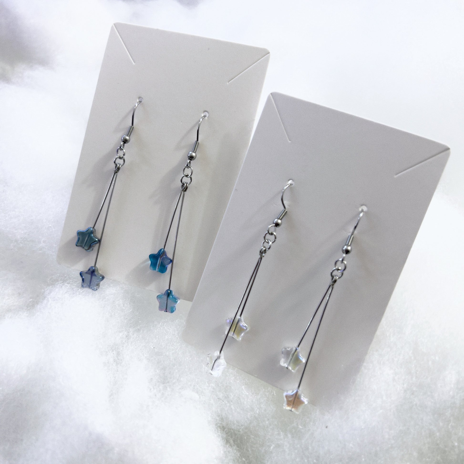 Two pairs of earrings next to each other, left with blue starry beads, and right with clear starry beads.